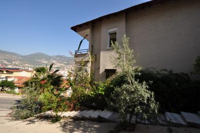 Alānijas īpašuma balkons ar flīžu grīdu, sarkaniem krēsliem un panorāmas skatu uz pilsētu un kalniem.