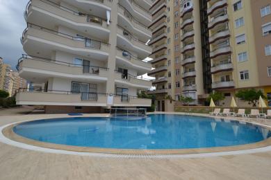 Alanya fastighet: Ljust vardagsrum och kök i öppen planlösning med vita skåp, klinkergolv och bekväma sittplatser.