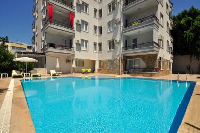Alanya'da hasır mobilyalar, parlak güneş ışığı ve şehir manzarası fonu ile rahatlatıcı bir atmosfere sahip balkon manzarası.