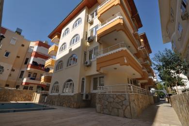 Habitación luminosa y vacía en Alanya con suelo de baldosas de terracota, ventana arqueada y paredes cálidas en tonos neutros.