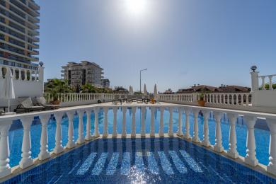 Alanya Immobilienansicht mit einem Tennisplatz mit Berg- und Gebäudeansichten unter blauem Himmel.