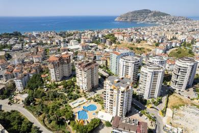Balcon de propriété à Alanya avec mobilier en osier, balustrade en verre et vue ensoleillée sur la ville.