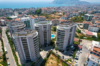 Lys Alanya leilighet stue med et moderne hvitt kjøkken, spisebord, komfortabel sofa og flislagt gulv.
