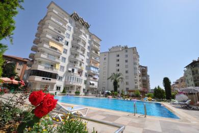 Sala de estar luminosa do apartamento em Alanya com acesso à varanda, pisos de cerâmica e vistas da cidade a partir de grandes janelas.