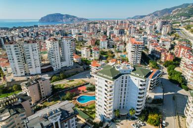 Alanya erkély fa asztallal, kő elemekkel, és panorámás városi és tengeri kilátással, ragyogó napsütésben.