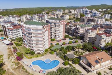 Balcón de propiedad en Alanya con muebles de mimbre, suelo de baldosas e impresionantes vistas al mar bajo una luz natural brillante.