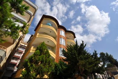 Alanya property balcony with wicker chairs, table, and wrought iron railing offering city views.