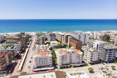 Alanya-Immobilienbalkon mit weißen Säulen, Fliesenboden und Sitzgelegenheiten im Freien mit Blick auf üppige tropische Anlagen.