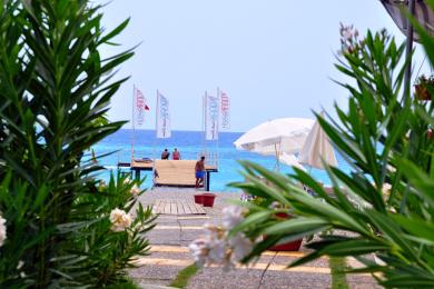 Lys Alanya balkon med kurvemøbler, glasbord og skydedøre med udsigt over moderne bygninger.