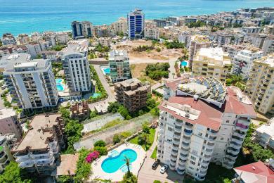 Alanya property balcony with wicker chairs, stone table, and bright, sunny views of nearby buildings.