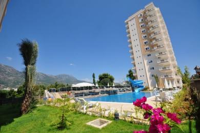 Salon de propriété à Alanya avec des canapés neutres, un revêtement de sol en carrelage et une cuisine américaine avec un éclairage chaleureux et accueillant.