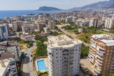 Nemovitost Alanya: Světlý, otevřený kuchyňský a obývací prostor se světlými dřevěnými skříňkami a pohodlnou koženou pohovkou.
