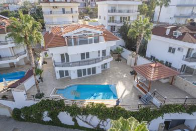 Außenansicht einer Villa in Alanya mit einem leuchtend blauen Swimmingpool, Palmen und einer sonnigen, luxuriösen Atmosphäre.