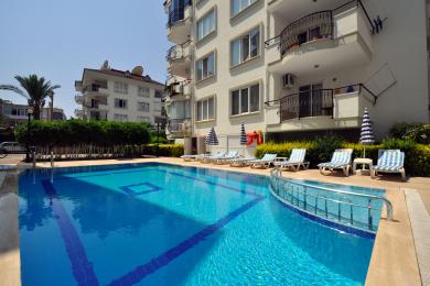 Alanya nekretnina dnevna soba s krem ​​sofom, foteljama, staklenim stolom i mekim prirodnim svjetlom.