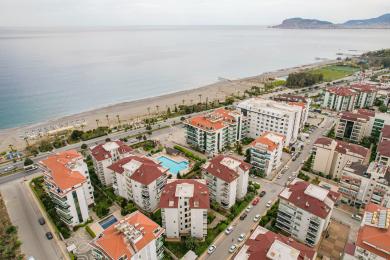 Alanya eiendom balkong med kurvmøbler, fliser og lys, luftig atmosfære med utsikt over frodig grøntområde.