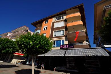 Lyst Alanya køkken med flisegulv, orange og creme farvede skabe og adgang til balkon, hvilket skaber en rummelig fornemmelse.