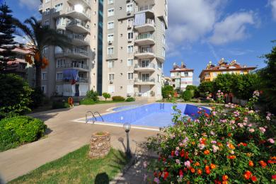 Alanya-Immobilienbalkon mit Glasgeländer bietet einen hellen Blick auf den angelegten Garten.