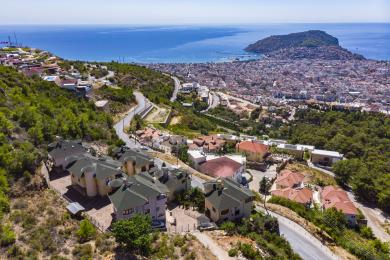 Vanjski izgled nekretnine u Alanji s bazenom, prugastim suncobranima i balkonom s pogledom na more.