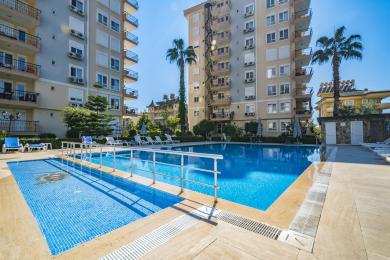 Lichte Alanya woonkamer met neutrale bank, fauteuil, houten tafels en tegelvloer, waardoor een gezellige sfeer ontstaat.