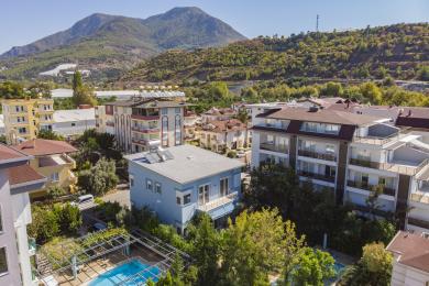 A espaçosa sala de estar em Alanya apresenta pisos de madeira, sofás de couro, lustres elegantes e luz suave e convidativa.