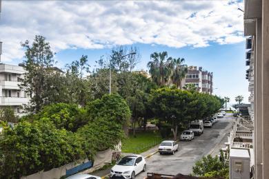 Proprietate în Alanya cu vedere de la balcon spre copaci verzi luxuriante și mașini parcate într-o zi însorită.