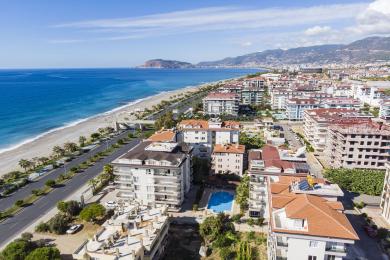 Φωτεινό μπαλκόνι της Αλάνια με γυάλινους τοίχους, ψάθινες καρέκλες και θέα στη θάλασσα, δημιουργώντας μια χαλαρωτική ατμόσφαιρα.