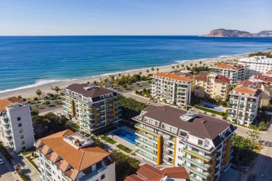 Luminoso soggiorno ad Alanya con divano, finestre a tutta altezza e splendida vista sul mare dal balcone.