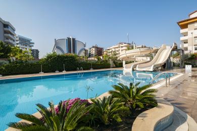 Gri bir kanepe, balkon erişimi, koyu renk perdeler ve modern beyaz mobilyalar içeren aydınlık Alanya oturma odası.