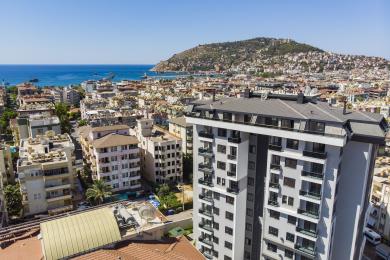 Šviesus Alanya būsto interjeras su marmurinėmis grindimis, laiptais ir dideliais langais, iš kurių atsiveria vaizdai į jūrą.