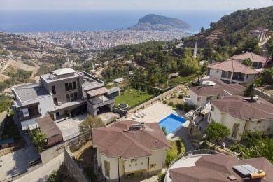 Alanya mulkidagi neytral divanlar, quyuq yog'och aksentlari va yorqin, tabiiy yorug'likka ega ochiq oshxonani o'z ichiga olgan yashash xonasi.