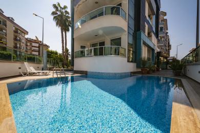De heldere woonkamer van dit appartement in Alanya beschikt over een moderne keuken, een grijze bank, een vloerkleed met patroon en glanzende tegelvloeren.