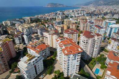 Alanya mulkidagi bej divan, to'q yog'och stol va yorug', havodor muhitga ega yashash xonasi.