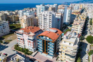 Alanya onroerend goed woonkamer met een beige bank, moderne kroonluchter en grote ramen met transparante gordijnen.