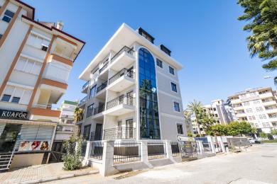 Svijetla kuhinja apartmana u Alanji s bijelim ormarićima, crnom pozadinom, mramornim podovima i velikim prozorima.