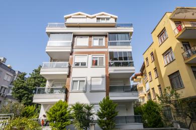 Alanya ingatlan: Világos, nyitott terű nappali modern, fehér konyhával, csempézett hátfallal és kényelmes, virágos fotellel.