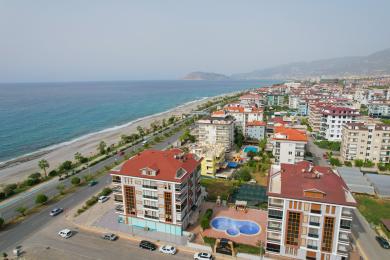 Lys Alanya stue med flislagte gulv, komfortable sitteplasser og et stort vindu med utsikt over byen.