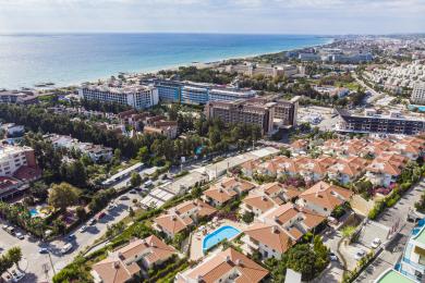 Alanya eiendom balkong med steinvegg, flislagt gulv, metallrekkverk og utsikt over byen under sterkt sollys.