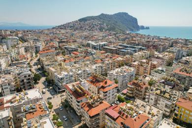 Svijetla dnevna soba apartmana u Alanji s podovima od pločica, udobnim sjedećim mjestima, blagovaonicom i ukrasnom umjetnošću na prozorima.