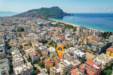 Alanya ingatlan erkélyén fonott bútorok, mintás csempepadló és egy zöld napernyő található az árnyékos szabadtéri élethez.