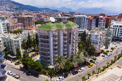 Alanya eign með svölum með flísalögðu gólfi, glerhandriði og útsýni yfir gróskumikil græn tré.