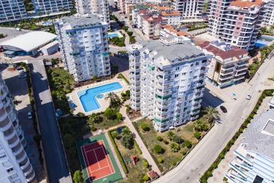 Vue de la propriété d'Alanya présentant une piscine, un court de tennis et des jardins paysagers sous un ciel lumineux et ensoleillé.