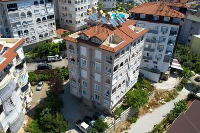 Varanda de Alanya com aberturas em arco, balaustrada branca, piso de cerâmica e vista para a cidade, criando uma atmosfera luminosa e arejada.