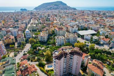 Balcone di proprietà ad Alanya con mobili in vimini, pavimento in piastrelle e vista sulla città sotto una luce naturale e brillante.