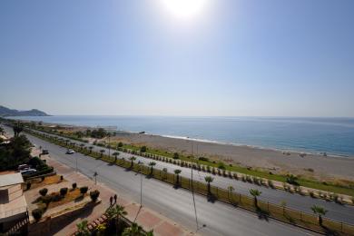 Vista da varanda da propriedade em Alanya, mostrando a praia, o Mar Mediterrâneo e a estrada costeira ensolarada.