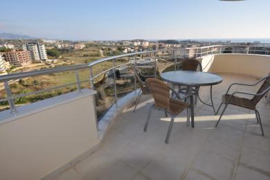 Alanya woning balkon met wicker meubilair, tegelvloeren en panoramisch uitzicht op de stad en de zee bij helder daglicht.