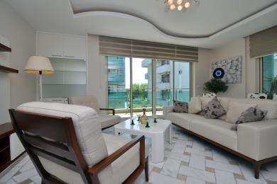 Luminoso salón en Alanya con suelos de mármol, muebles blancos y grandes ventanas que ofrecen una vista.