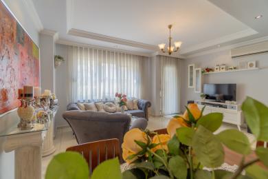 De woonkamer van dit pand in Alanya is voorzien van een zachte grijze bank, transparante gordijnen en een heldere, luchtige sfeer.