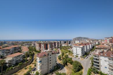 Výhľad na nehnuteľnosť v Alanyi s panorámou mesta, Stredozemným morom a jasnou modrou oblohou.