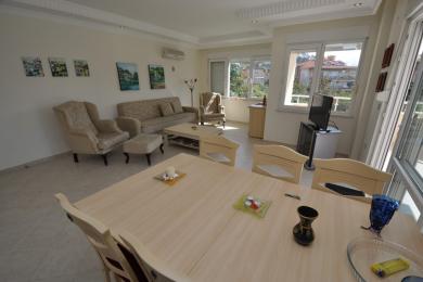 Sala de estar luminosa em Alanya com móveis neutros, mesa de jantar de madeira e vistas de grandes janelas.