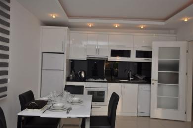 Alanya property kitchen featuring glossy white cabinets, a black backsplash, a dining table, and a bright, modern atmosphere.